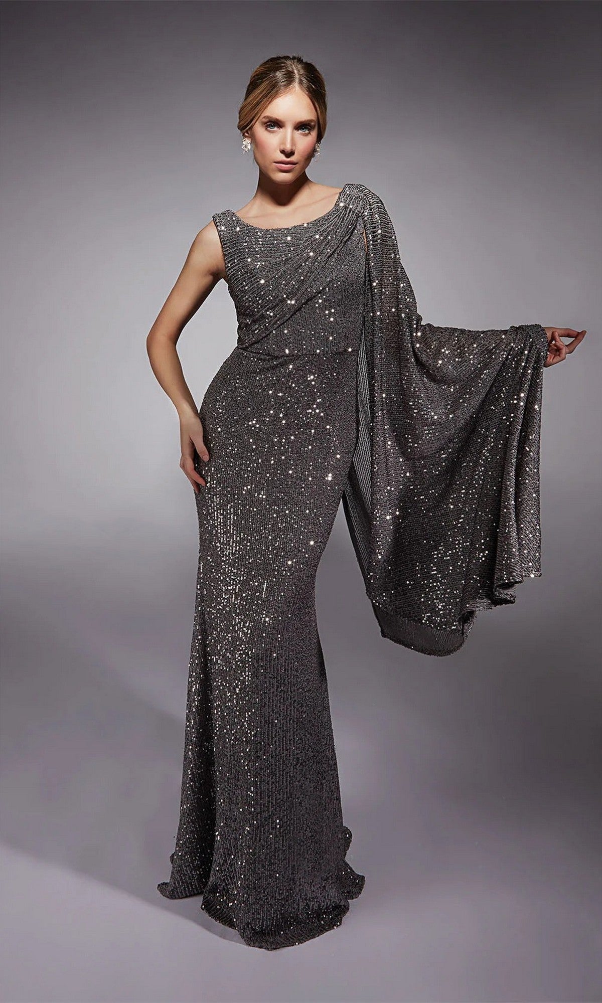 A woman models the Alyce 27718 long formal dress—floor-length with sequins and a one-shoulder cape sleeve—against a neutral background.